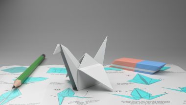 Handen die een origamikraan vouwen van wit papier op een houten tafel
